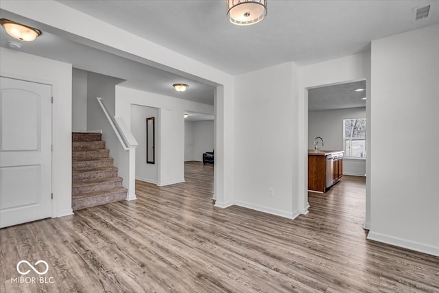 unfurnished living room with stairway, wood finished floors, visible vents, and a sink