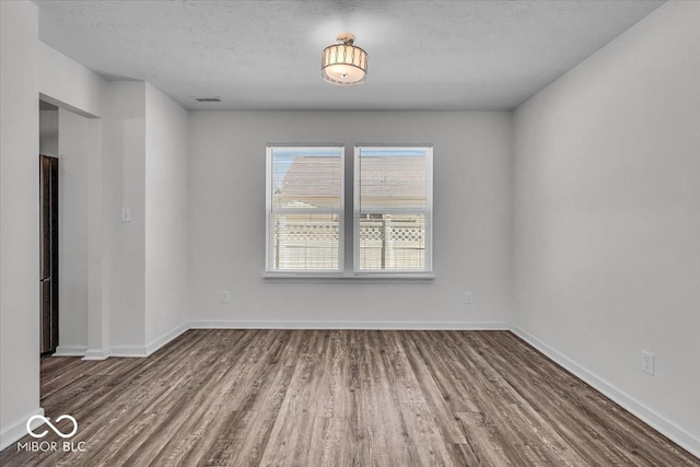 spare room with visible vents, baseboards, a textured ceiling, and wood finished floors