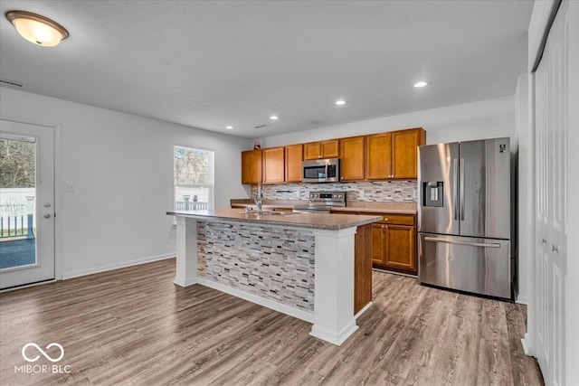 kitchen with stainless steel appliances, decorative backsplash, light wood-style flooring, and brown cabinetry