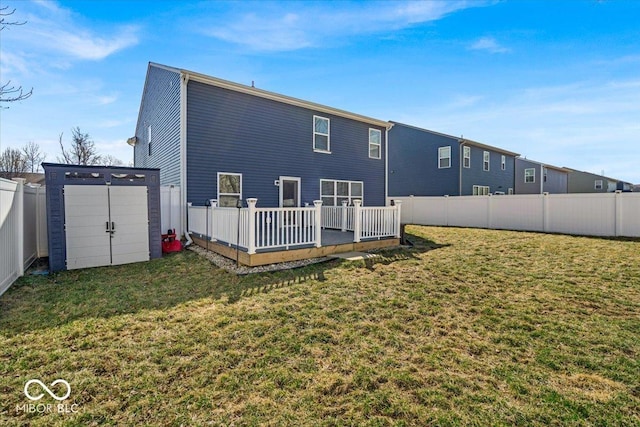 back of property with a wooden deck, a yard, a fenced backyard, an outdoor structure, and a storage unit