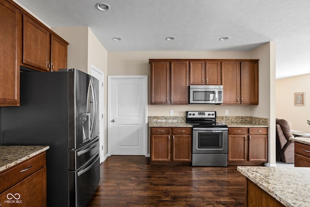 kitchen featuring stainless steel appliances, light stone countertops, and dark wood finished floors