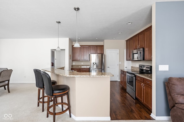 kitchen with light stone counters, baseboards, appliances with stainless steel finishes, a kitchen bar, and decorative light fixtures