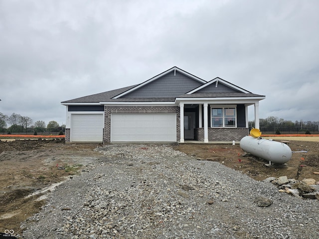 view of front of property featuring covered porch, brick siding, dirt driveway, and an attached garage