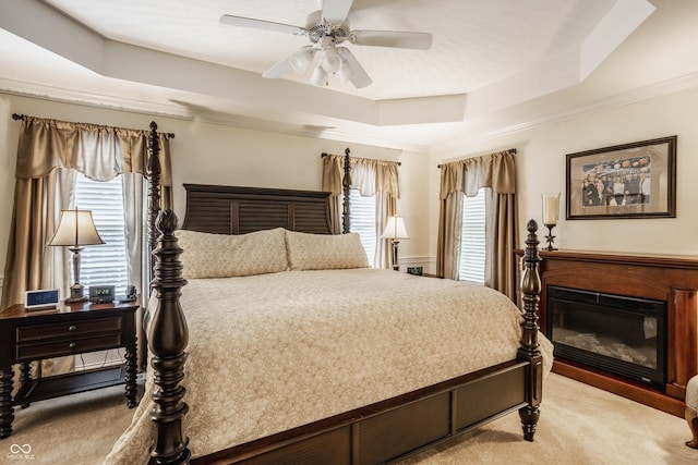 bedroom featuring light carpet, a glass covered fireplace, multiple windows, and a raised ceiling