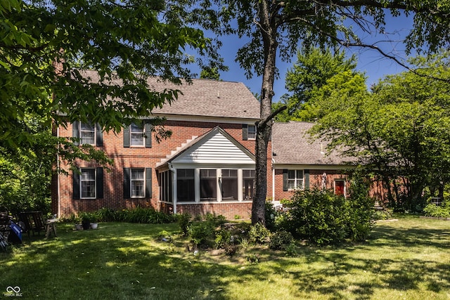 back of property featuring a yard, brick siding, and a sunroom