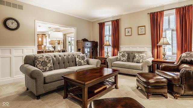 living room with visible vents, light carpet, wainscoting, crown molding, and a decorative wall