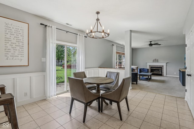 dining area featuring ceiling fan with notable chandelier, light tile patterned flooring, a wealth of natural light, and a fireplace