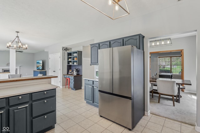 kitchen with light colored carpet, light countertops, freestanding refrigerator, a notable chandelier, and light tile patterned flooring