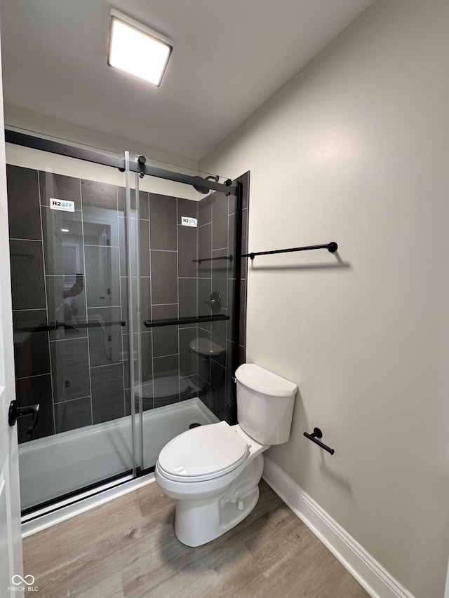 full bathroom with baseboards, toilet, wood finished floors, and a shower stall