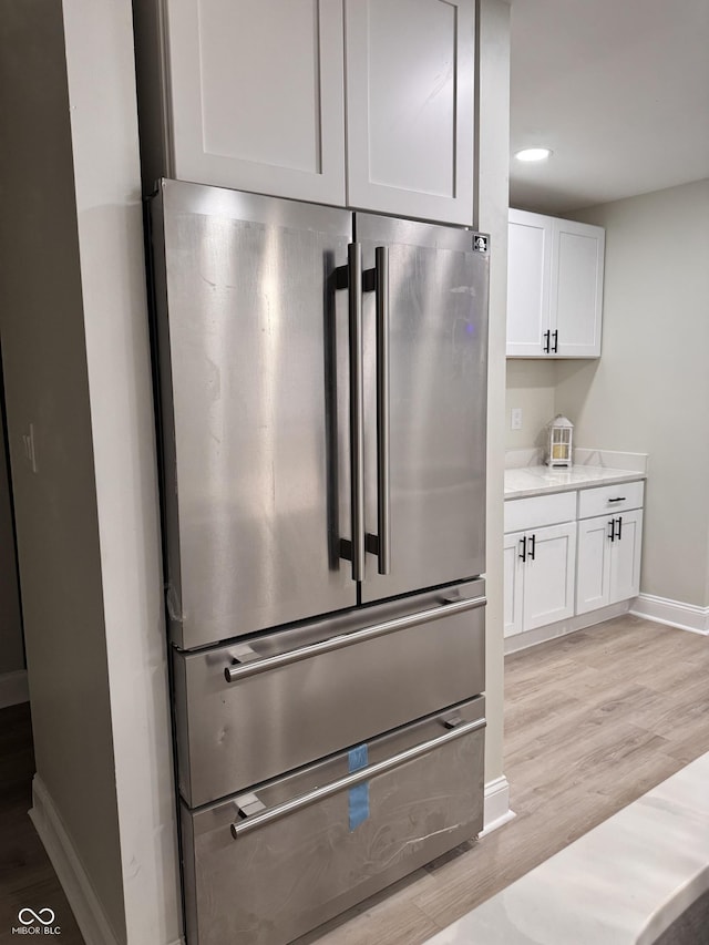 kitchen with baseboards, light stone countertops, light wood-style flooring, freestanding refrigerator, and white cabinets