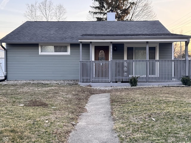 view of front of house featuring a front yard, a chimney, covered porch, and a shingled roof