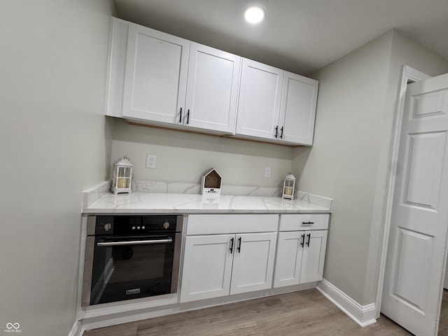 kitchen featuring light stone counters, white cabinets, oven, and baseboards