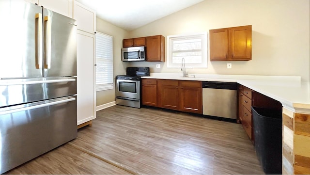 kitchen featuring lofted ceiling, appliances with stainless steel finishes, light wood-style floors, brown cabinetry, and a sink