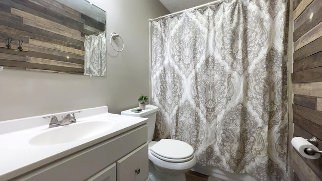 full bath with wooden walls, vanity, and toilet