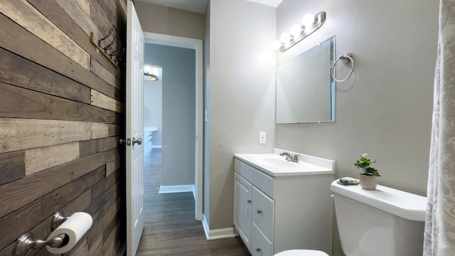 half bath with wooden walls, baseboards, toilet, wood finished floors, and vanity