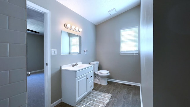 half bath with vanity, wood finished floors, baseboards, vaulted ceiling, and toilet