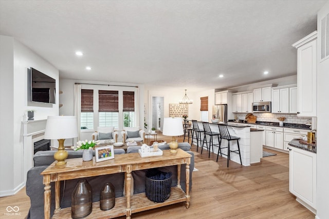 living room featuring visible vents, light wood-style flooring, recessed lighting, a fireplace, and a notable chandelier