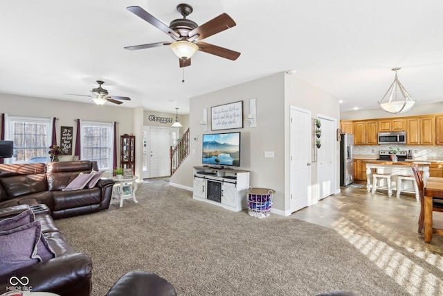 carpeted living room with stairway, baseboards, and ceiling fan