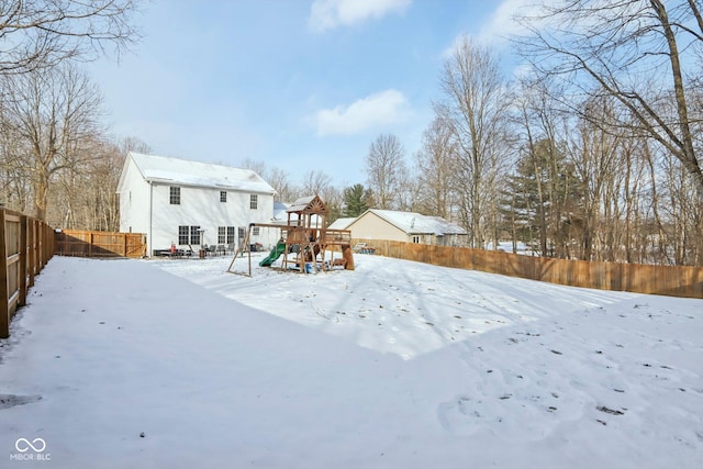 snowy yard featuring a playground and a fenced backyard