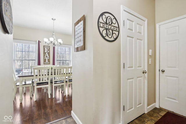 corridor with baseboards, a notable chandelier, and dark wood finished floors