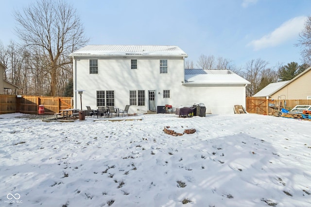 snow covered rear of property featuring metal roof and fence