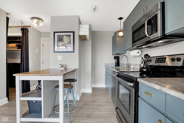 kitchen with a sink, appliances with stainless steel finishes, light wood finished floors, baseboards, and light stone countertops