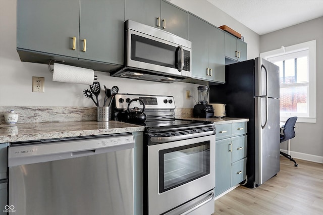 kitchen with light stone counters, light wood-style floors, baseboards, and appliances with stainless steel finishes