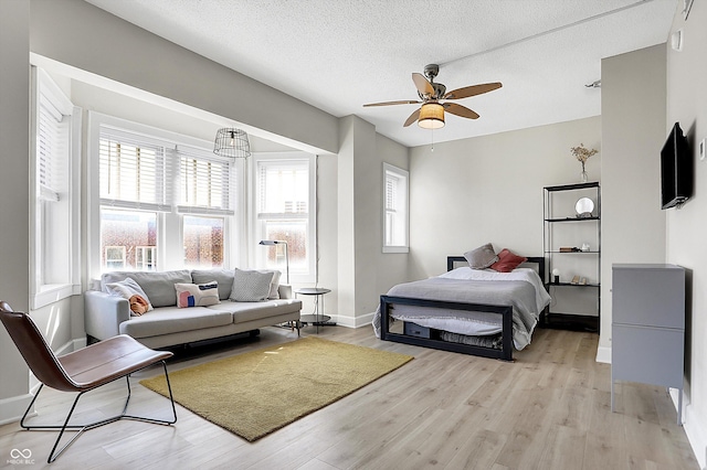 bedroom with light wood-style flooring, a textured ceiling, baseboards, and ceiling fan