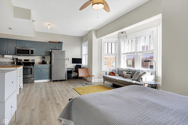 bedroom with baseboards, light wood finished floors, freestanding refrigerator, ceiling fan, and a textured ceiling