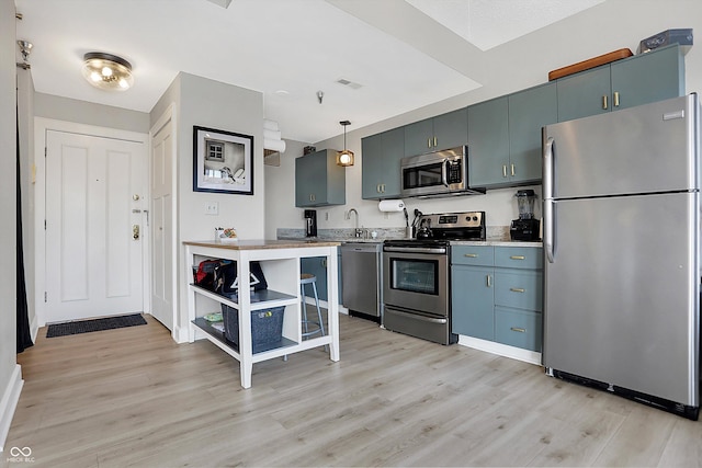 kitchen with light wood finished floors, pendant lighting, light countertops, stainless steel appliances, and a sink