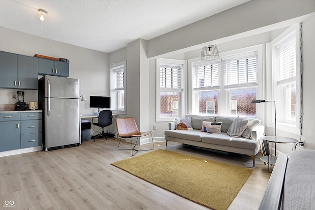 living room featuring light wood-type flooring, baseboards, a textured ceiling, and a healthy amount of sunlight