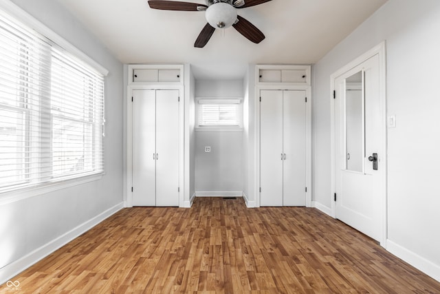 unfurnished bedroom with a ceiling fan, baseboards, light wood-type flooring, and two closets