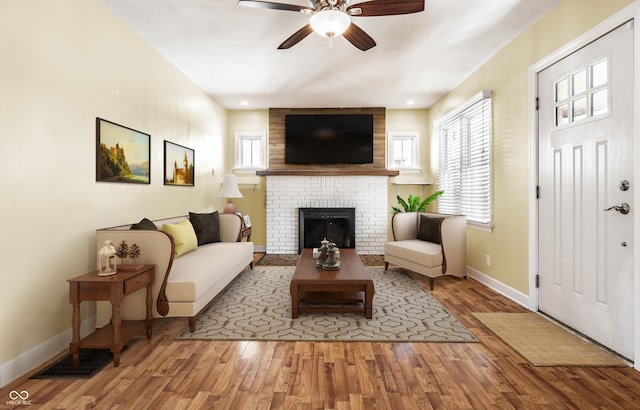 living room featuring ceiling fan, baseboards, wood finished floors, and a fireplace