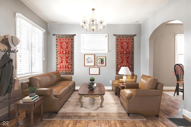 living room featuring visible vents, a notable chandelier, wood finished floors, arched walkways, and baseboards