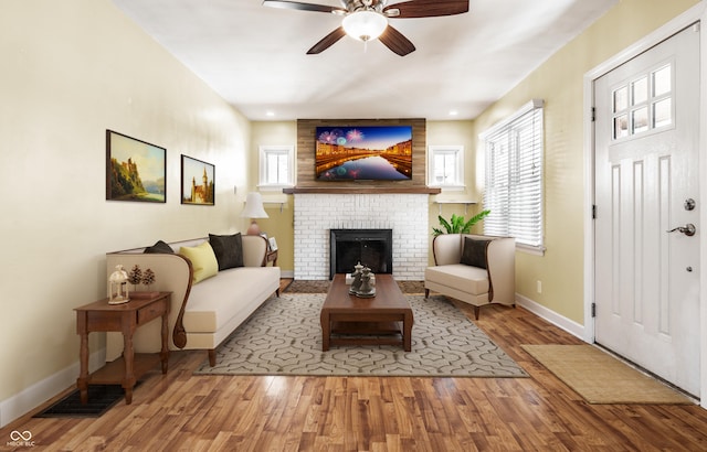 living room featuring visible vents, a brick fireplace, ceiling fan, baseboards, and wood finished floors