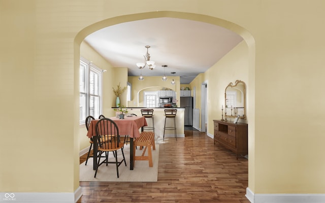 dining area with an inviting chandelier, wood finished floors, baseboards, and arched walkways