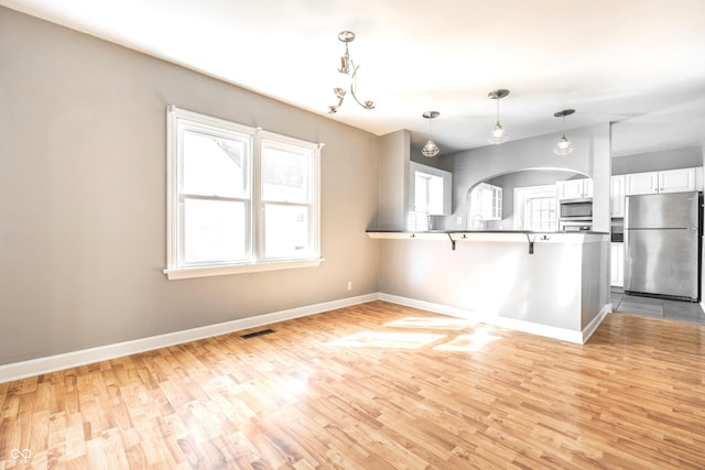 kitchen with baseboards, a peninsula, stainless steel appliances, light wood-style floors, and white cabinetry