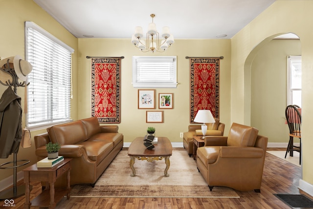 living area with visible vents, wood finished floors, arched walkways, baseboards, and a chandelier