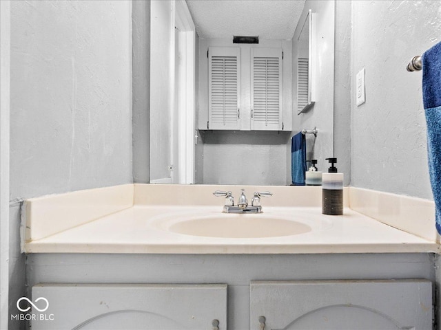 bathroom with a textured ceiling, vanity, and a textured wall