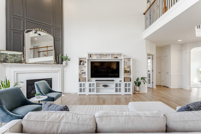 living room with a glass covered fireplace, wood finished floors, a towering ceiling, and decorative columns