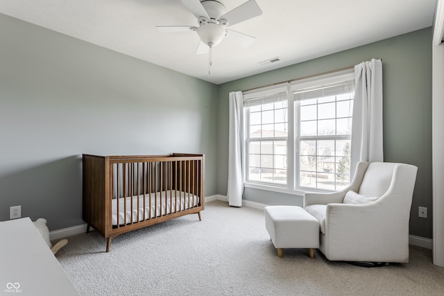 carpeted bedroom featuring a crib, baseboards, visible vents, and a ceiling fan