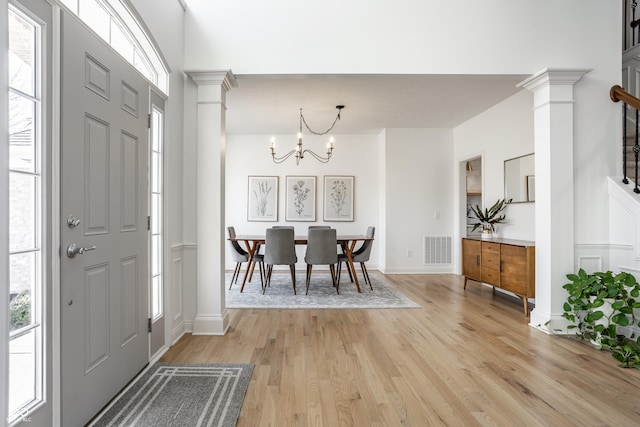 entrance foyer with light wood finished floors, visible vents, baseboards, a chandelier, and ornate columns