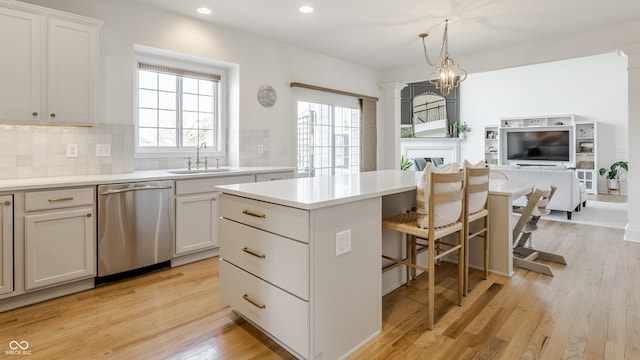 kitchen featuring light wood finished floors, a sink, decorative backsplash, stainless steel dishwasher, and a center island