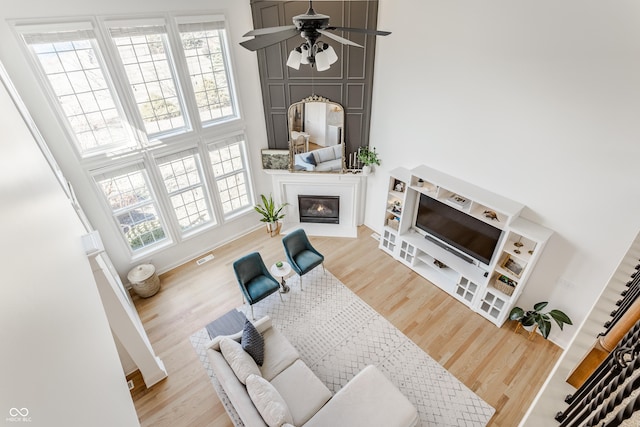 living room with visible vents, baseboards, wood finished floors, a glass covered fireplace, and a ceiling fan