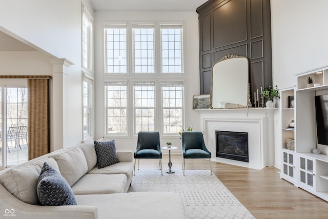 living area featuring a fireplace with flush hearth, a healthy amount of sunlight, a high ceiling, and light wood-style floors