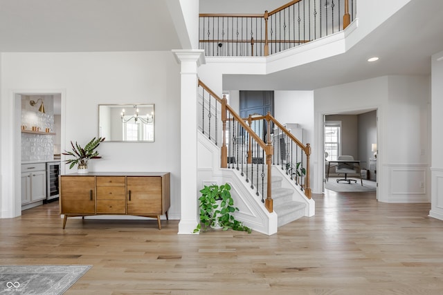 foyer with light wood finished floors, beverage cooler, stairway, a decorative wall, and ornate columns