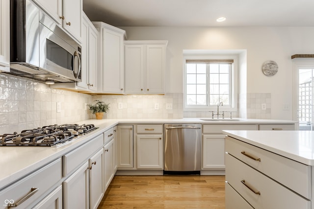 kitchen featuring light wood-type flooring, light countertops, stainless steel appliances, white cabinetry, and a sink