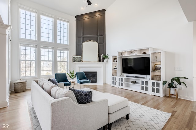 living room featuring light wood-type flooring, baseboards, a high ceiling, and a glass covered fireplace