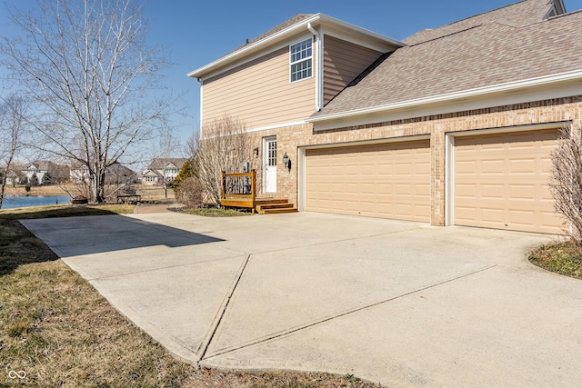 view of home's exterior featuring driveway, roof with shingles, an attached garage, a water view, and brick siding