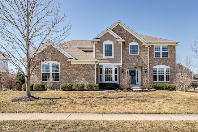 view of front of house with brick siding, a front lawn, and roof with shingles